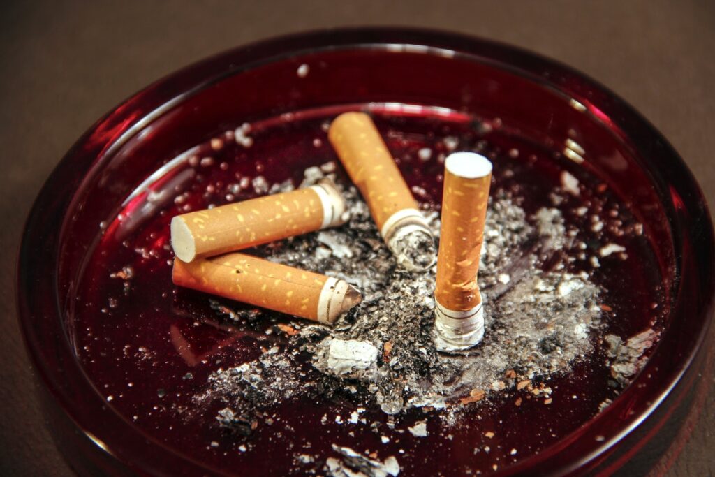 An amber–colored glass ashtray filled with used cigarette butts along with their ashes.