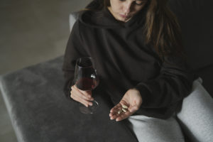 Addicted woman drinking red wine and take a pills